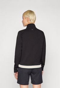 Black sweatshirt with a high collar, ribbed hem featuring beige and light gray stripes, and a smooth texture. Shorts are dark with pockets.