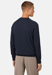 Temno modra bombažna majica s dolgimi rokavi, rebrastim ovratnikom in robom ter preprostim dizajnom. Gladka tekstura brez vzorcev ali poudarkov.