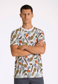 Vit t-shirt med kort ärm som har ett färgglatt tropiskt frukt- och lövmönster i gröna, orange och bruna nyanser.