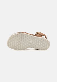 Brun sandalbunn med teksturert hvit gummisåle med zikk-zakk-mønster. Justerbare stropper og detaljer med gullfarget spenne.