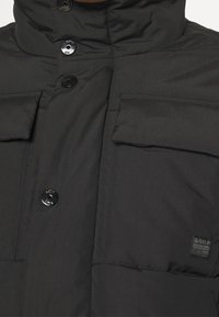 Svart vadderad jacka fram med stora kläpfickor, tryckknappar och G-Star Originals Raw Denim-logotyp på den nedre högra fickan.