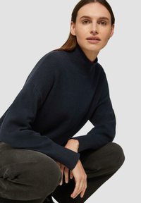 Dunkelblauer Wollrollkragenpullover mit geripptem Kragen und Bündchen, in lockerem Schnitt und gestrickter Textur, kombiniert mit dunkelgrauen Hosen.