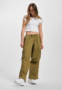 Oliven grøn cargo-bukser med elastisk talje, sidelommer og snøredetaljer, parret med en hvid cropped t-shirt og hvide sneakers.