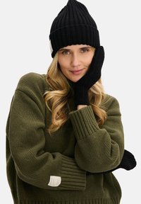 Czarna dziana czapka z wysokim prążkowanym wzorem, w komplecie z czarnymi prążkowanymi rękawiczkami. Oliwkowozielony, luźny sweter o fakturowanej strukturze z detalem w postaci metki.