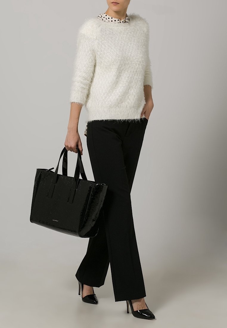 Valkoinen pörröinen neule, mustat suorat housut, musta kiiltävä käsilaukku ja mustat korkokengät. Neuleessa on kuvioitu kaulus.