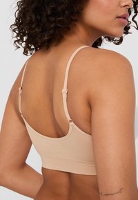 Beige bralette med justerbara band, sömlös design, mjukt tyg och en slät textur. Har subtil branding på baksidan.
