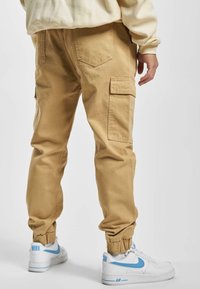 Khaki spodnie cargo z elastycznymi mankietami, kieszeniami bocznymi i luźnym krojem, w połączeniu z białymi sneakersami z niebieskimi akcentami.