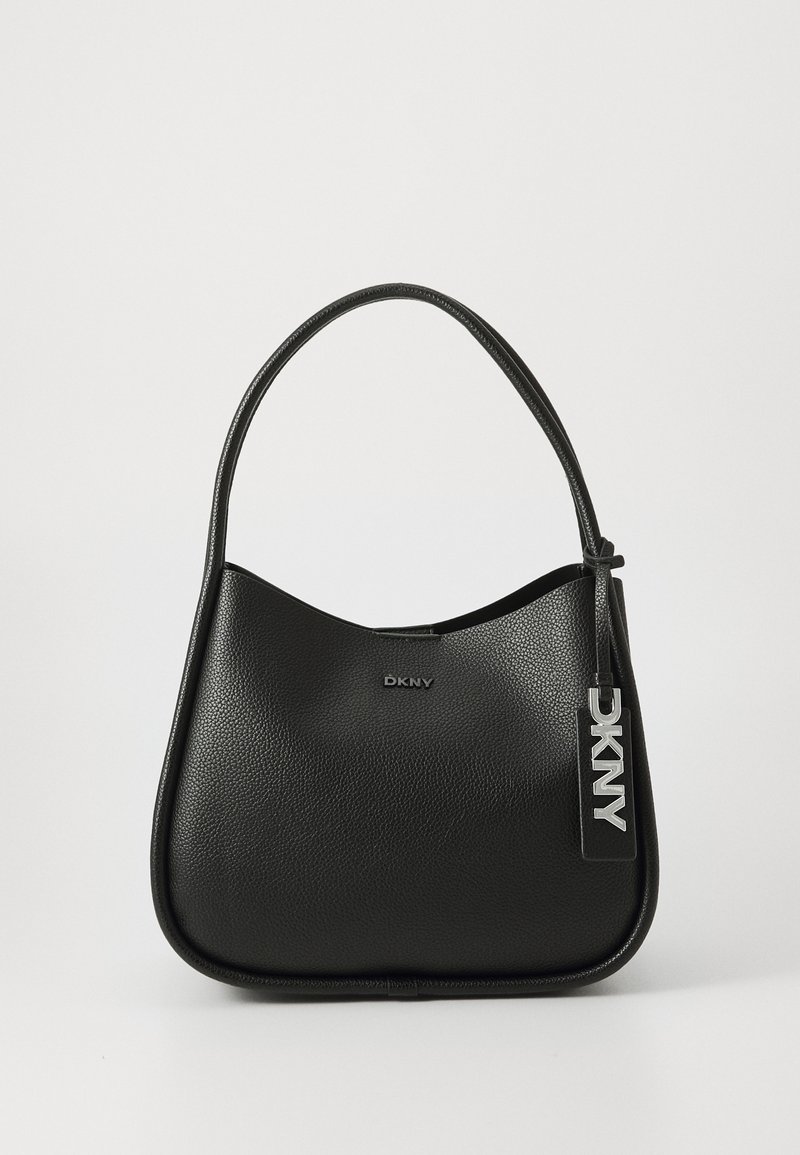 Sac à main en cuir noir texturé avec une bandoulière unique, bord supérieur incurvé et une étiquette suspendue avec des lettres DKNY argentées.