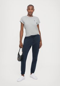 Tricou gri cu mânecă scurtă, având un logo mic, combinat cu pantaloni joggeri bleumarin, prevăzuți cu buzunare laterale și șnur, completat cu teniși albi.