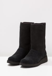 Czarne zamszowe botki na płaskiej gumowej podeszwie, o zaokrąglonym nosku i miękkim górnym brzegu. Brak widocznych elementów metalowych czy wzorów.