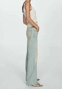 Vaaleansiniset korkeavyötäröiset farkut, joissa on haalentunut ombre-efekti, yhdistettynä kermaiseen toppiin. Mallilla on kädet taskuissa ja hänellä on jalassa teräväkärkiset kengät.