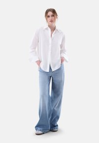 Weißes Hemd mit langen Ärmeln, kombiniert mit hellblauen weiten Jeans, die einen lockeren Sitz und eine weiche Stofftextur aufweisen.