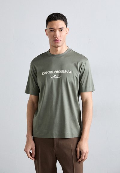 Olivgrünes Baumwoll-T-Shirt mit kurzen Ärmeln und Rundhalsausschnitt; zeigt das Logo "EMPORIO ARMANI Milano" in Weiß auf der Brust.