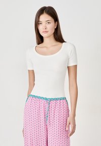 Top bianco a maniche corte con scollatura a girocollo, abbinato a pantaloni rosa con motivo e cordino turchese in vita.