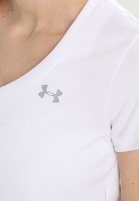 Bílé tričko s krátkým rukávem a výstřihem do V, vyrobené z hladké tkaniny, s malým šedým logem Under Armour na levé straně hrudi.