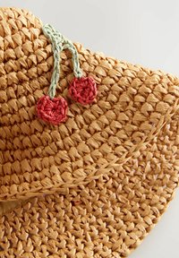 Chapeau de paille à large bord, texture tissée naturelle, et tresse verte avec deux cerises au crochet rouges comme accent.