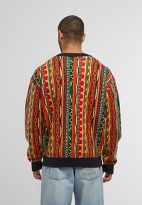 Kleurrijke gebreide trui met een gedurfde patroon van rode, groene, gele en zwarte strepen. Ribgebreide manchetten en zoom met een losse pasvorm.