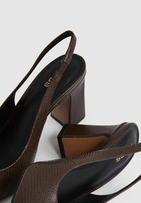 Zapatos de tacón en color marrón, con diseño texturizado, que cuentan con un interior negro y tacones en forma cuadrada con detalles en marrón claro.