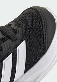 Scarpa da ginnastica nera con tomaia in mesh, dettagli bianchi e tessuto strutturato. Presenta una suola robusta e un design strutturato per supporto.