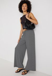 Calças largas com riscas pretas e brancas combinadas com um top preto justo. O conjunto inclui uma mala preta de ombro e sandálias planas pretas.