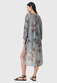 Vestito lungo e leggero in tessuto azzurro trasparente con motivo floreale in tonalità rosa e verde. Presenta maniche lunghe e spacchi laterali.