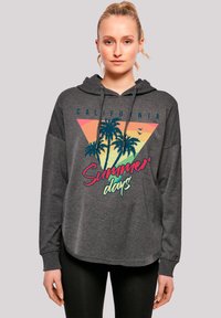 Young woman wearing a dark gray hoodie with palm trees and "California Summer days" text, standing against a plain background.