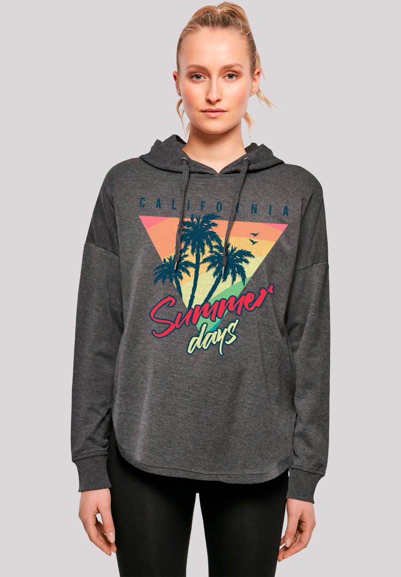 Young woman wearing a dark gray hoodie with palm trees and "California Summer days" text, standing against a plain background.