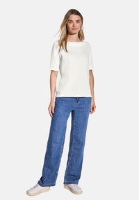 Top corto bianco testurizzato a maniche corte abbinato a jeans a gamba larga blu e scarpe da ginnastica bianche, con un semplice scollo rotondo e una vestibilità comoda.