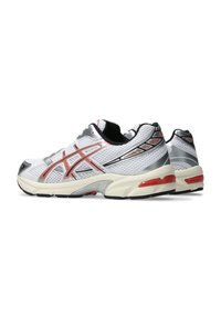 Scarpe da ginnastica bianche con una tomaia in mesh, dettagli argentati, rifiniture rosse e una suola ammortizzata con una suola nera e motivi testurizzati.