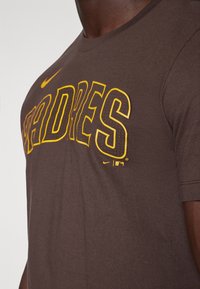 Brun bomull t-shirt med "PADRES" i fet gul skrift. Inkluderar en liten Nike-logotyp och MLB-emblem på den nedre framsidan. Korta ärmar.