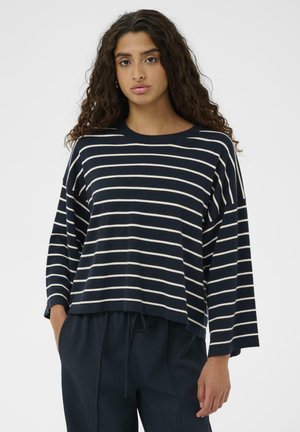 Marineblå stribet pullover med cremefarvede striber, afslappet pasform, brede ærmer, ribbet hals, tekstureret strikket stof, båret over mørke bukser.