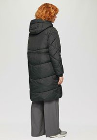 Zwarte pufferjas met een capuchon, voorzien van een gewatteerd patroon en lange mouwen. Draag het over grijze wijde broek en sneakers.