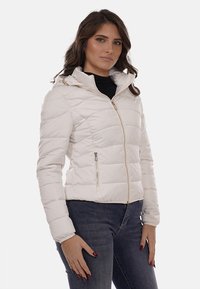 Giacca imbottita bianca con zip frontale, cappuccio e due tasche con zip. Presenta un design a righe cucite orizzontali e dettagli in hardware color oro.