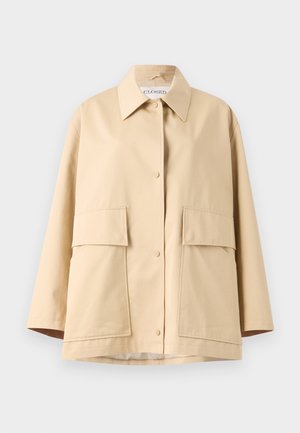 Bēšs žakets, kas izgatavots no gludas auduma ar klasisku apkakli, divām lielām priekšējām kabatām un brīvu piegriezumu. Aizverams ar redzamām poga.