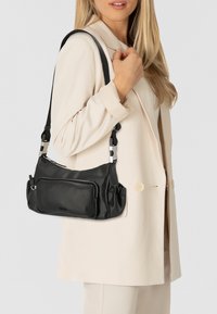 Bolso de hombro de cuero negro con correa ajustable y bolsillos con cremallera. Presenta lados fruncidos y un diseño elegante y minimalista.
