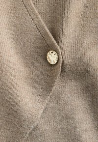 Cardigan beige a coste in maglia con tessuto strutturato e bottone rotondo decorativo dal design marmorizzato.