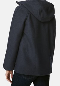 Cappotto con cappuccio di colore navy realizzato in tessuto testurizzato; presenta una silhouette dritta, tasche laterali e una chiusura con zip parzialmente visibile.