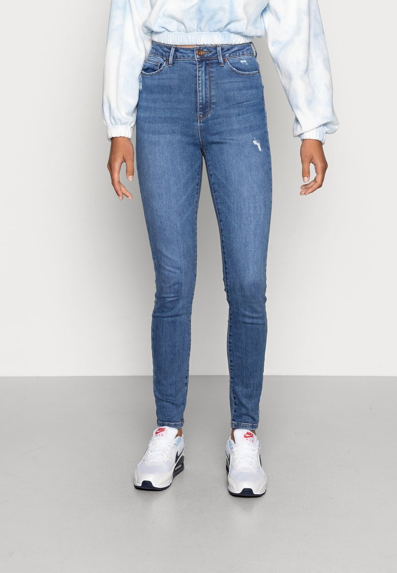 Jeans ajustados en denim azul medio con un ligero desgaste y roturas. Diseño de cintura alta con bolsillos frontales y cierre de botón.