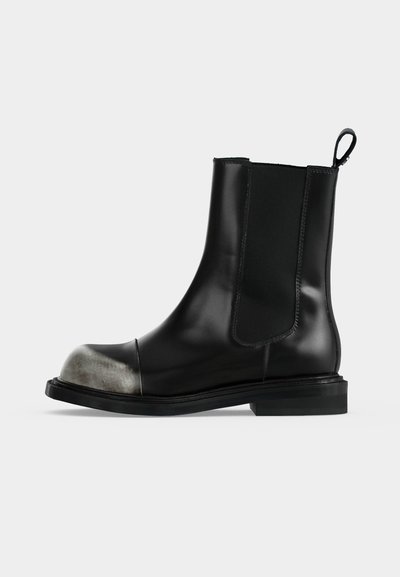 Bottine en cuir noir avec panneaux latéraux élastiques, languette à l’arrière et embout métallique argenté usé.
