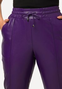 Pantalon en cuir violet avec une taille élastique et un cordon de serrage, doté de poches latérales et d'une texture lisse.