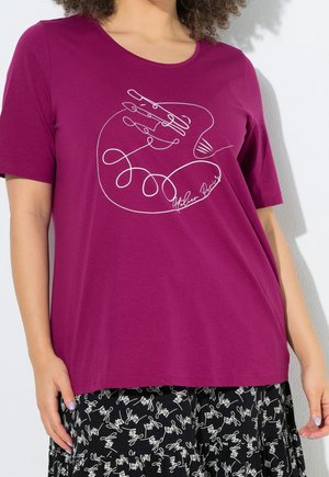 Femme portant un haut violet à manches courtes avec un motif main en ligne continue blanche et une jupe noire avec un motif d’écriture blanche.