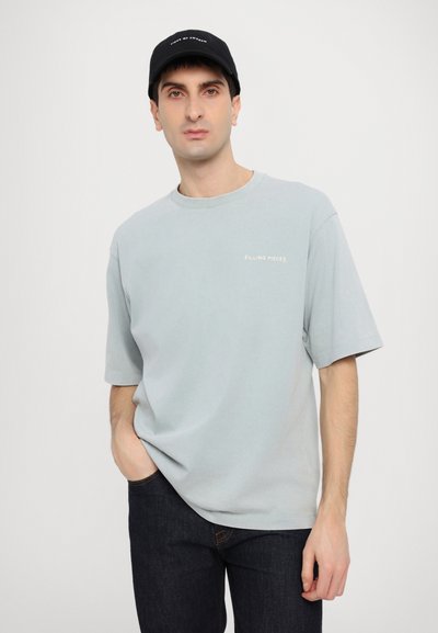Světle modré tričko s krátkým rukávem a kulatým výstřihem, s bílým nápisem "FILLING PIECES". Kombinováno s tmavými džíny a černou kšiltovkou.