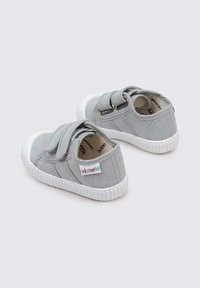 Baskets en toile grises avec semelles en caoutchouc blanc et accents au niveau des orteils. Dotées d'une seule sangle Velcro et d'un logo "victoria" coloré sur le côté.