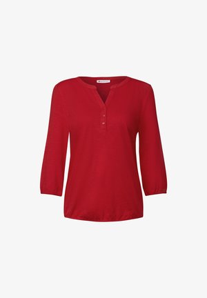 Červená blůza s dlouhým rukávem a výstřihem do V, na krku se třemi knoflíky. Lehká tkanina, mírně nařasené rukávy a volný střih.