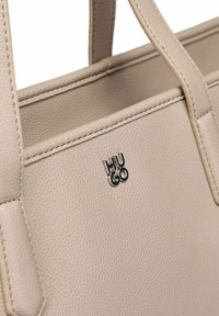 Borsa tote in pelle beige con superficie testurizzata, dotata di due manici e di un logo "HUGO" argento sul davanti.