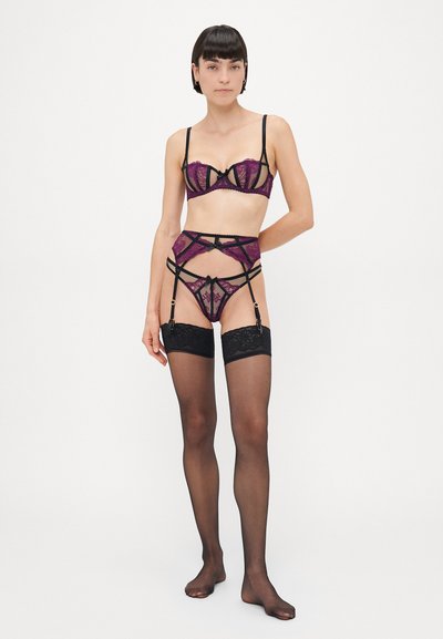 Een kanten lingerieset in paars en zwart, met doorschijnende panelen, ingewikkelde patronen en verstelbare bandjes; inclusief een jarretel en kousen tot boven de knie.