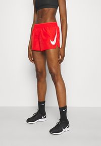 Shorts de sport rouges avec un logo Nike blanc, taille élastique et coupe ample, assortis à des baskets Nike noires et des chaussettes.
