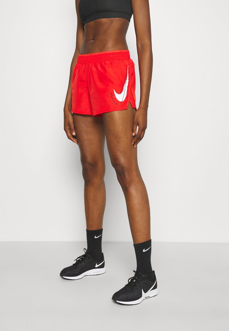 Shorts de sport rouges avec un logo Nike blanc, taille élastique et coupe ample, assortis à des baskets Nike noires et des chaussettes.