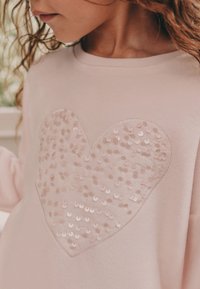 Felpa rosa chiaro con un grande cuore realizzato in paillettes. Tessuto morbido con un dettaglio del cuore testurizzato e lucido e scollo a girocollo.