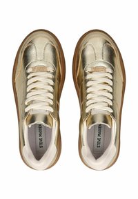 Sneaker dorati metallizzati con finitura liscia, lacci bianchi e suola in gomma marrone chiaro. Presenta il logo sulla linguetta e accenti a contrasto.